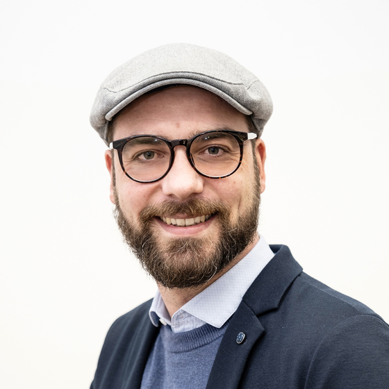 Öffnet den Servicebereich "Über diese Seite". Bildbeschreibung: Porträt Marc Partetzke. Ausschnitt von Kopf bis Bauch mit weißem Hintergrund. Er sitzt leicht gedreht und blickt lächelnd in die Kamera. 