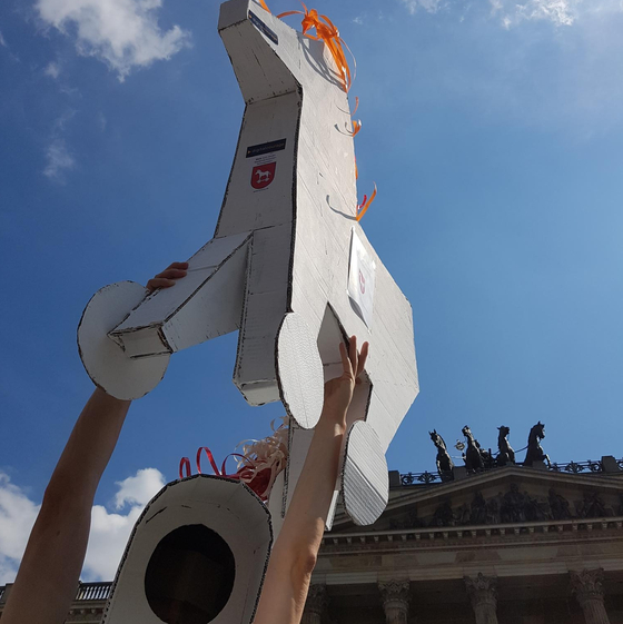 Alternativporträt von Digitalcourage Ortsgruppe Braunschweig. Es ist ein Trojanisches Pferd aus Pappe in den Händen einer Person abgebildet. Im Hintergrund sieht man ein teil des Brandenburger Tors und den klaren Himmel.