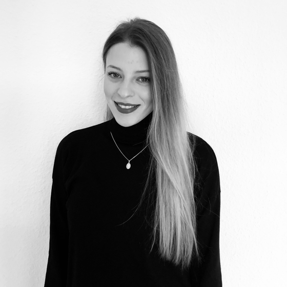 Öffnet den Servicebereich "Über diese Seite". Bildbeschreibung: Porträt Daphne Cetta. Ausschnitt von Kopf bis Taillier mit einfarbigen Hintergrund. Sie steht leicht gedreht und lächelt in die Kamera. 