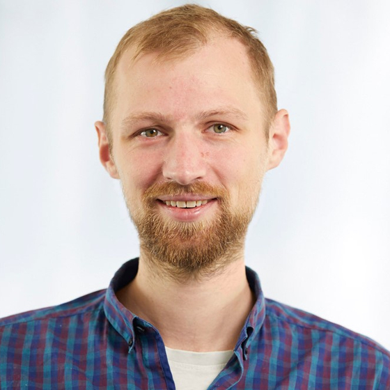 Porträt Marus Lauter. Ausschnitt von Kopf bis Schulter mit einfarbigen Hintergrund. Er blickt in die Kamera und lächelt.  