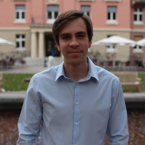 Öffnet den Servicebereich "Über diese Seite". Bildbeschreibung: Porträt Stefan Steiger. Man sieht ihn bis zur Hüfte. Erträgt ein Hemd und blickt in die Kamera. Im Hintergrund sieht man eine Häuserwand und aufgestellte Sonnenschirme.