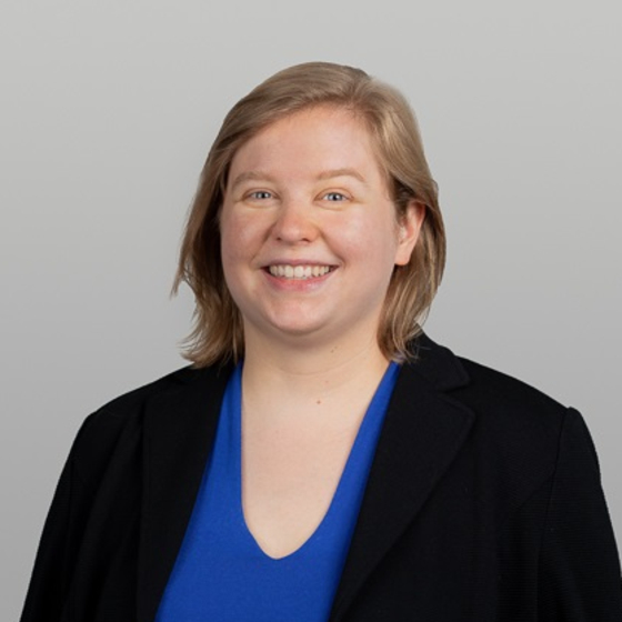 Porträt Karolin Busse. Ausschnitt Kopf und Oberkörper. Der Hintergrund ist einfarbig und sie lächelt frontal in die Kamera. 